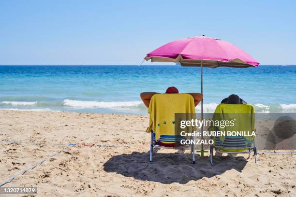 parasol, two chairs and towels on sand beach while tourists having bath in sea in summer - beach sunbathing spain 個照片及圖片檔