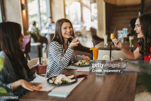 three young cheerful female friends enjoying lunch together at restaurant - restaurant women friends lunch stock pictures, royalty-free photos & images