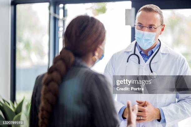 doctor discussing with patient in hospital lobby - mask confrontation stock pictures, royalty-free photos & images