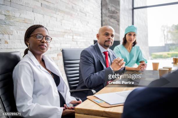 hospital staff listening to administrator in boardroom meeting - board room stock pictures, royalty-free photos & images