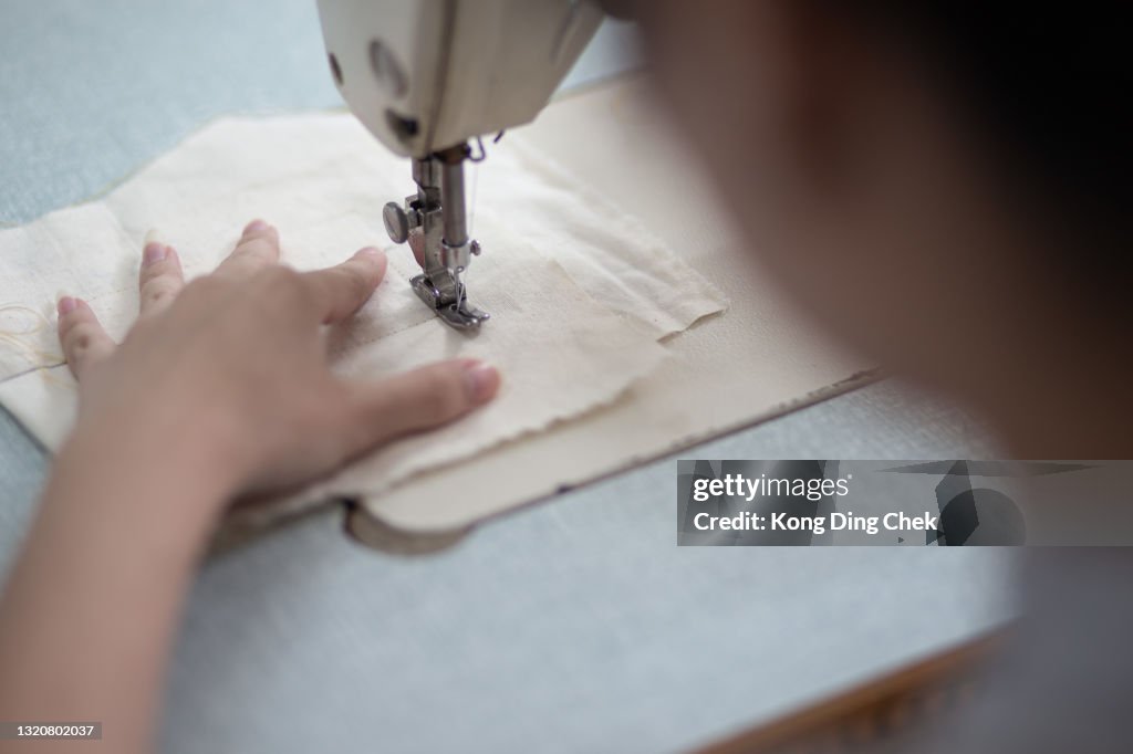 Close up Asian Chinese female fashion college student sewing clothing using sewing machine at college workshop