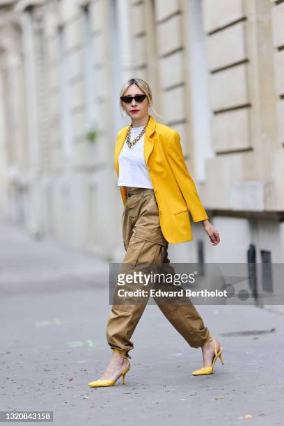 Emy Venturini wears black vintage sunglasses, a gold large chain necklace, a white Ipsilonparis t-shirt, a yellow oversized vintage blazer jacket, a...