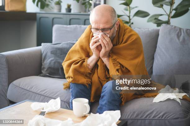 kranker mann sitzt auf einem sofa im zimmer - sinus stock-fotos und bilder
