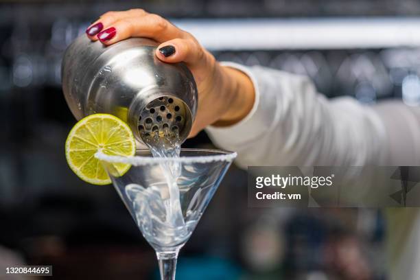 女調酒師將瑪格麗塔飲料倒入不鏽鋼雞尾酒搖床的玻璃杯中。 - 瑪格麗特 個照片及圖片檔