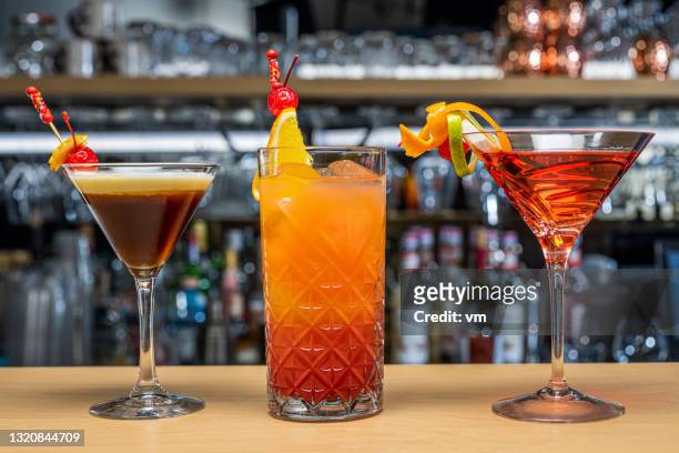 colorful cocktails waiting for you. glasses with drink standing on wooden bar counter. - tequila sunrise stock pictures, royalty-free photos & images