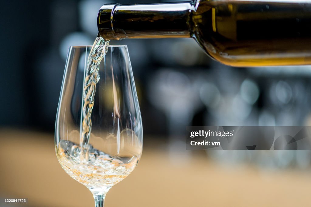 Pouring glass of wine. Serving white wine in transparent wine glass.