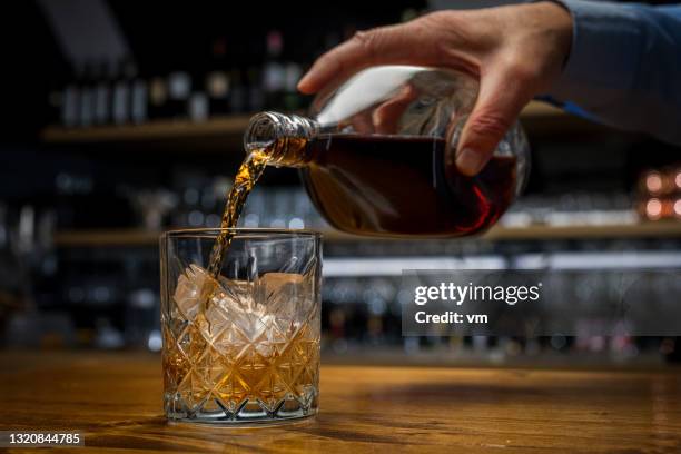 homme préparant la boisson, versant le vieux whisky écossais dans le verre debout sur une table en bois. - whisky photos et images de collection