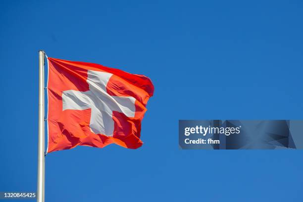 swiss flag with blue sky - schweizer flagge stock-fotos und bilder