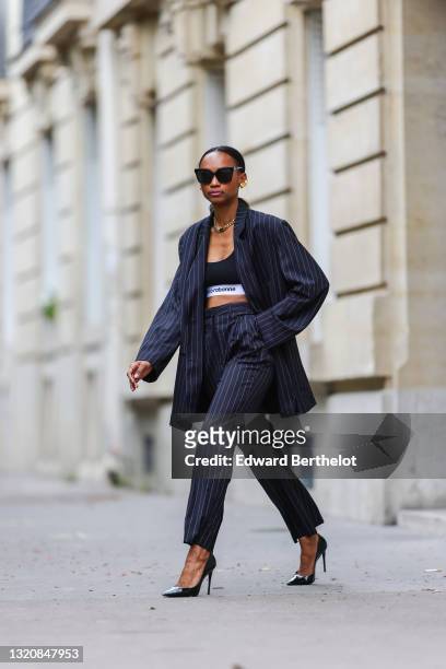 Emilie Joseph wears black sunglasses, golden earrings / earcuffs by Merbabe, a gold large chain necklace with thick cuban links by Merbabe, a black...