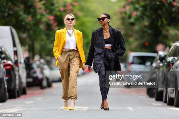 Emy Venturini wears black vintage sunglasses, a gold large chain necklace, a white Ipsilonparis t-shirt, a yellow oversized vintage blazer jacket, a...
