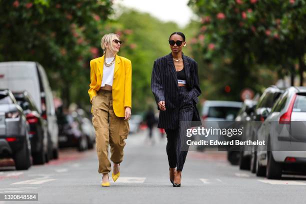 Emy Venturini wears black vintage sunglasses, a gold large chain necklace, a white Ipsilonparis t-shirt, a yellow oversized vintage blazer jacket, a...