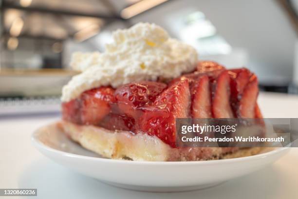 selective focus, close-up view at traditional german sliced fresh strawberry cake tart or pie on topped with whipped cream, and defocused background of white interior room. - restaurant düsseldorf stock pictures, royalty-free photos & images