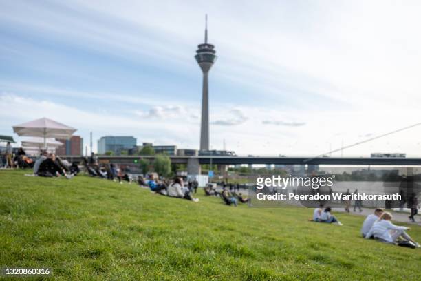 selective and low angle view at grass and defocus background, crowd of people sit, hang out and enjoy sunny day on park at promenade riverside of rhine river and background of rhine tower. - rivier gras oever stockfoto's en -beelden