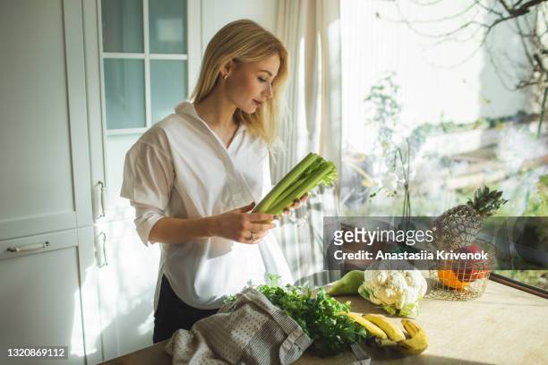 beautiful woman unpacks a full fabric bag with fruits and vegetables on the kitchen. - gemüse einkaufen stock-fotos und bilder