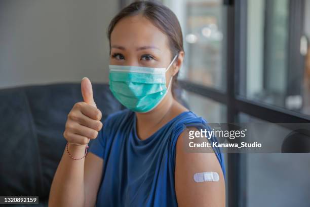 proud asian woman giving thumbs up after receiving a covid-19 vaccine - covid 19 vaccine stock pictures, royalty-free photos & images