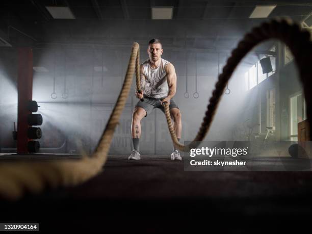 determined male athlete exercising with battle ropes in a gym. - white rope stock pictures, royalty-free photos & images