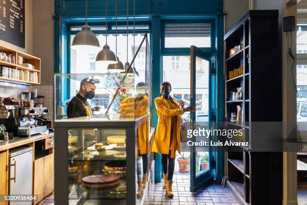 woman visiting a small coffee shop during pandemic - manteau jaune photos et images de collection
