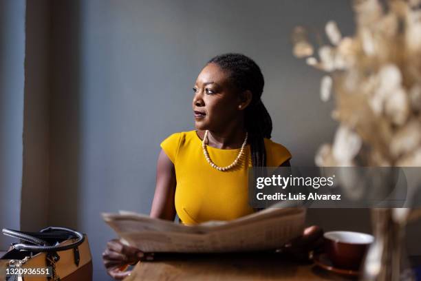 woman with newspaper sitting at cafe looking away - business news stock pictures, royalty-free photos & images