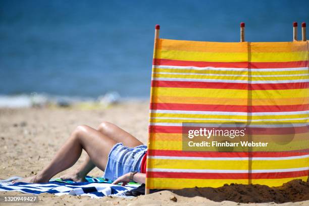 Woman's legs are seen behind a windbreak people enjoy the sunshine on the beach on May 31, 2021 in Bournemouth, England.