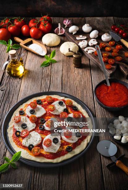 pizza italiana preparazione salsa di pomodoro e mozzarella cruda sull'impasto crudo della pizza con ingredienti - oliva nera foto e immagini stock