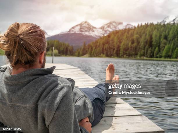 junger mann entspannt sich auf seepier bei sonnenuntergang, liegend - freizeit und hobbys stock-fotos und bilder