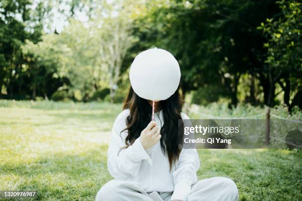 young woman holding cotton candy in the park - gesicht verstecken stock-fotos und bilder