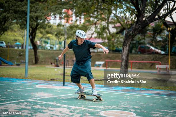 asian guy skateboarding in a park - schlägersport stock-fotos und bilder