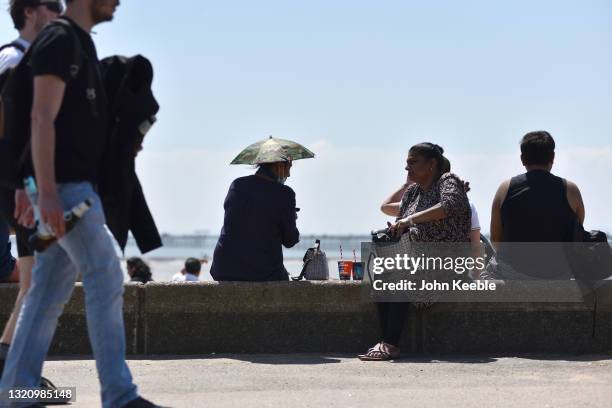 Woman wearing a sun shade umbrella hat sits on the seawall during the warm sunny weather at Jubilee beach on May 31, 2021 in Southend, England....
