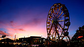 Ferris Wheel at Sunset with electric lights and carnival games and Rides in Image Purple and Pink Sunset
