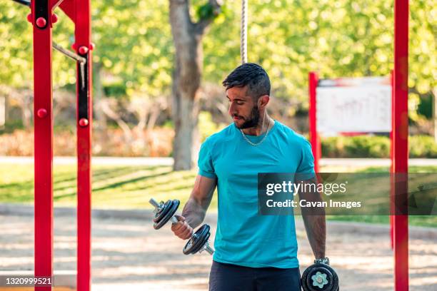 dark-haired athlete with beard training with dumbbells in a park. outdoor fitness concept. - musculation des biceps photos et images de collection