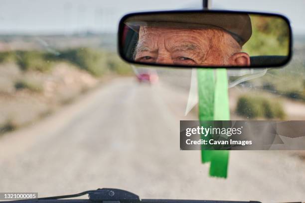 view from the rearview mirror of a car of an elderly man driving - car mirror stock-fotos und bilder