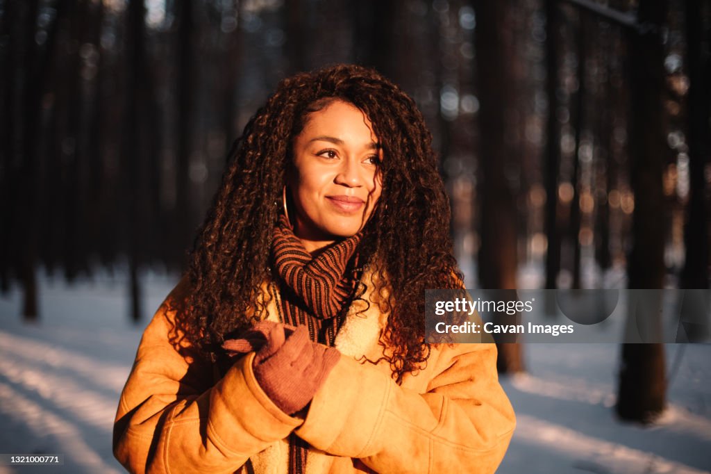 Happy young woman looking at sun standing in park during winter