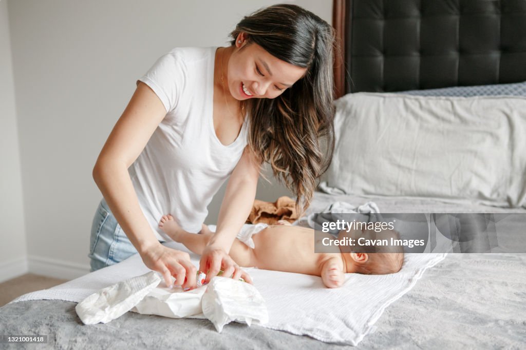 Asian busy mother changing diaper clothes for newborn baby son at home