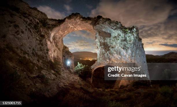 the silhouette of a man illuminates two large stone arches - flashlight stock-fotos und bilder