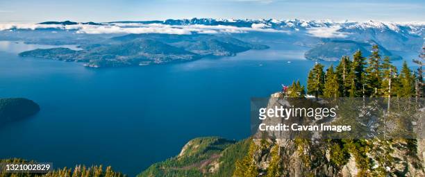 panoramic view of hiker standing on mountain summit, vancouver b.c. - inlet stock pictures, royalty-free photos & images