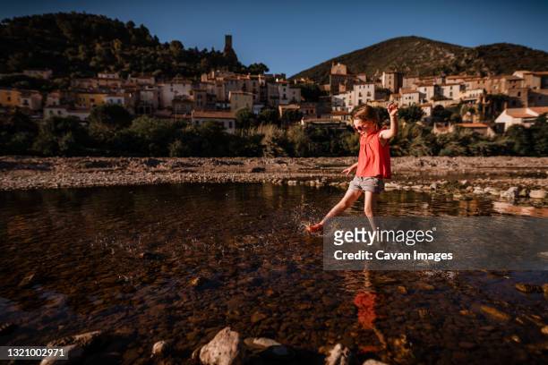 girl splashes water in river in france with village in background - kids at river photos et images de collection