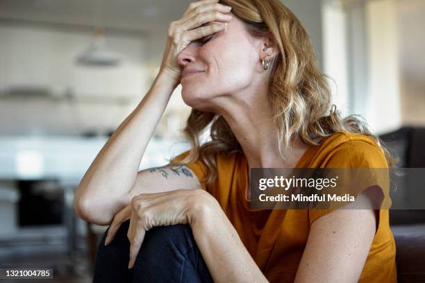 porträt einer weinenden frau mit denkhänden im gesicht, während sie drinnen sitzt - mourner stock-fotos und bilder