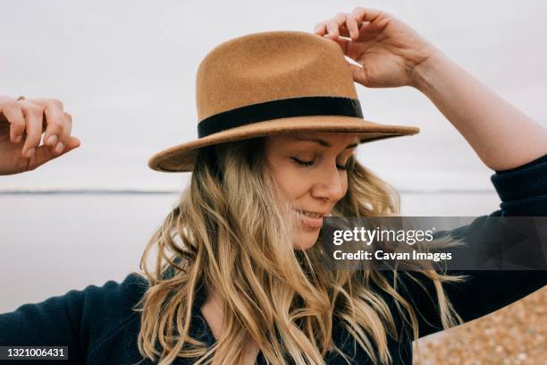 woman stood at the beach with wind blowing her hair and eyes closed - shiny wavy hair stock pictures, royalty-free photos & images