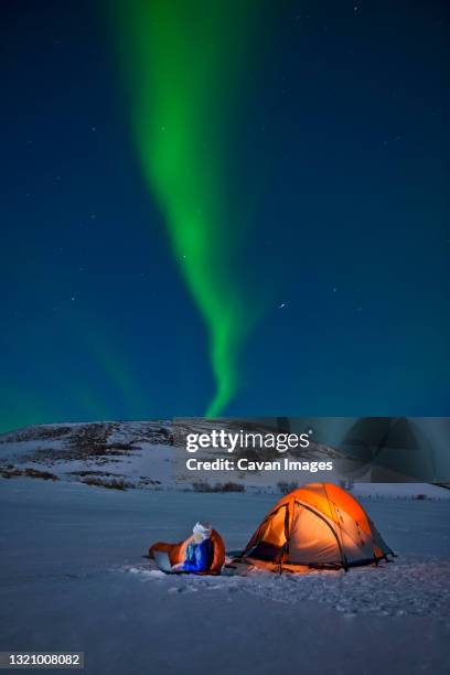 scientist sits outside of her tent with northern lights in the sky - northern lights iceland stockfoto's en -beelden