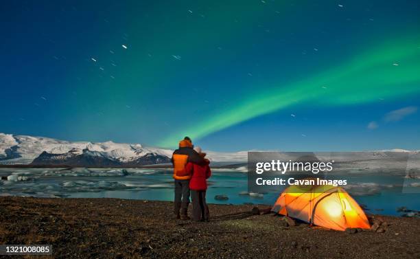 couple outside of their tent looking at northern lights in the sky - camp site stock-fotos und bilder