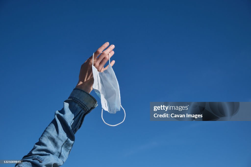 Hand throwing a mask in the air as a sign of freedom after receiving the vaccine, happiness for the end of the pandemic, holidays without a mask, end of covid-19, normal life post-pandemic, e