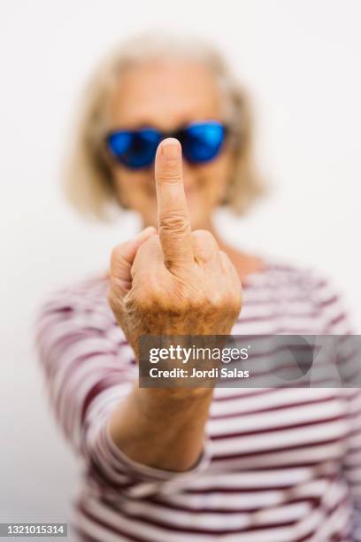 senior woman with dark sunglasses showing her middle finger - schocktaktik stock-fotos und bilder