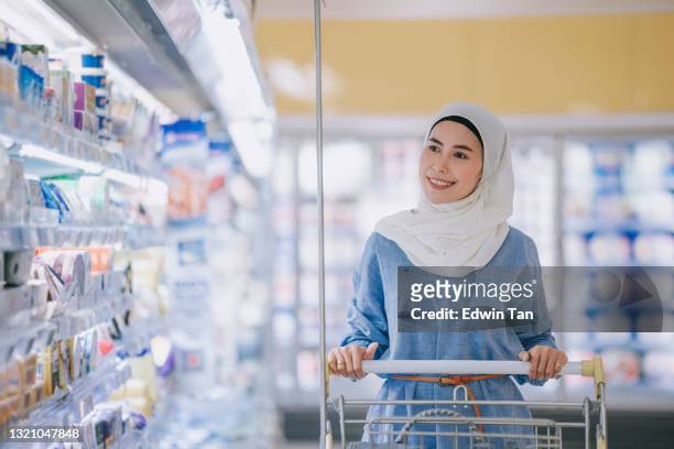 modern malay woman with hijab and modest clothing shopping buying at refrigerated section in supermarket during weekend - asian woman shopping grocery stock pictures, royalty-free photos & images
