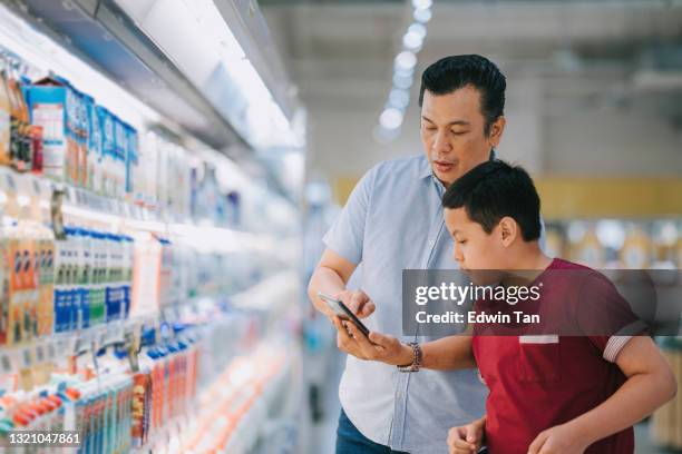 medio volwassen maleisische vader en zoon die herbruikbare het winkelen zak dragen die in supermarkt tijdens weekend winkelen - malaysia father and son stockfoto's en -beelden