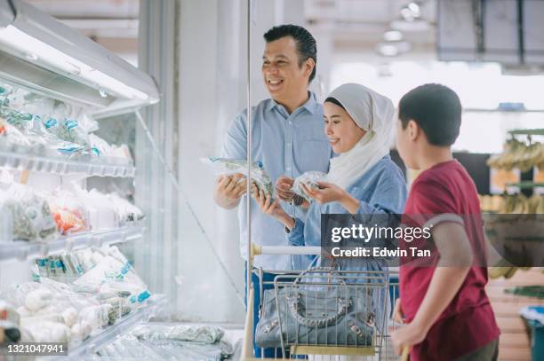 malay familie 2 eltern und sohn mit einkaufswagen wahl kauf gemüse in kühlbereich im supermarkt am wochenende - asian family shopping stock-fotos und bilder