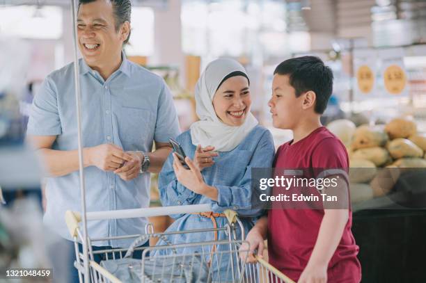 malay family 2 parent and son with smart phone shopping cart choosing buying vegetables at refrigerated section in supermarket during weekend - malay couple stock pictures, royalty-free photos & images