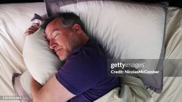 mature man in bed hugging his pillow with a satisfied expression - above view of man sleeping on bed stock pictures, royalty-free photos & images