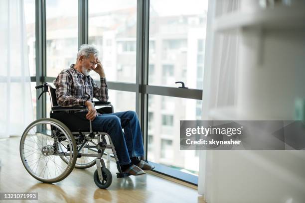 lonely senior man in a wheelchair by the window at home. - pandemic loneliness stock pictures, royalty-free photos & images