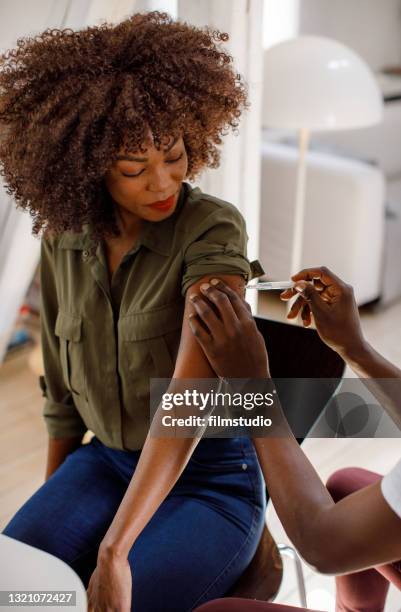 young woman receives a covid-19 vaccine dose from a healthcare worker at home - woman injecting stock pictures, royalty-free photos & images