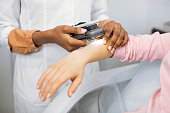 Doctor dermatologist examining birthmarks and moles on a female patient's hand. Close up cropped image of examination of birthmarks with modern device, using light and phone application and camera.